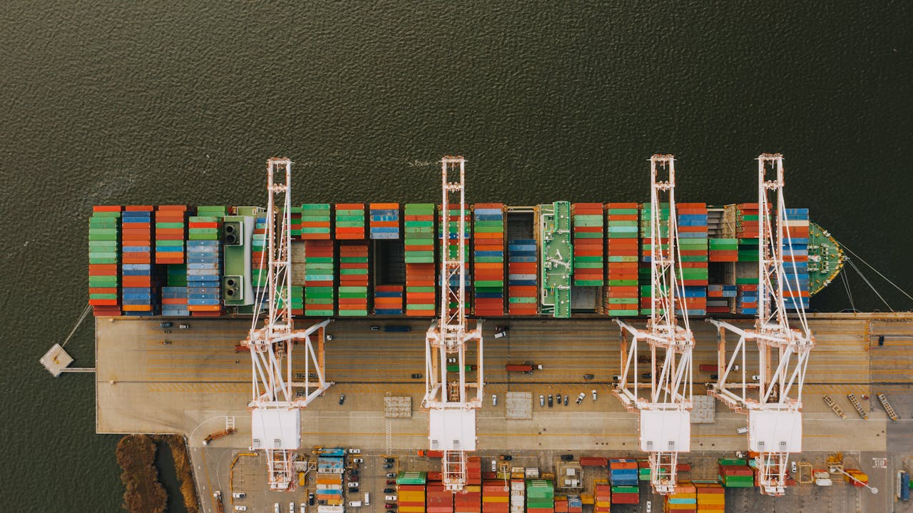 Drone view of long ship with many cargo near pier with steel lifting cranes